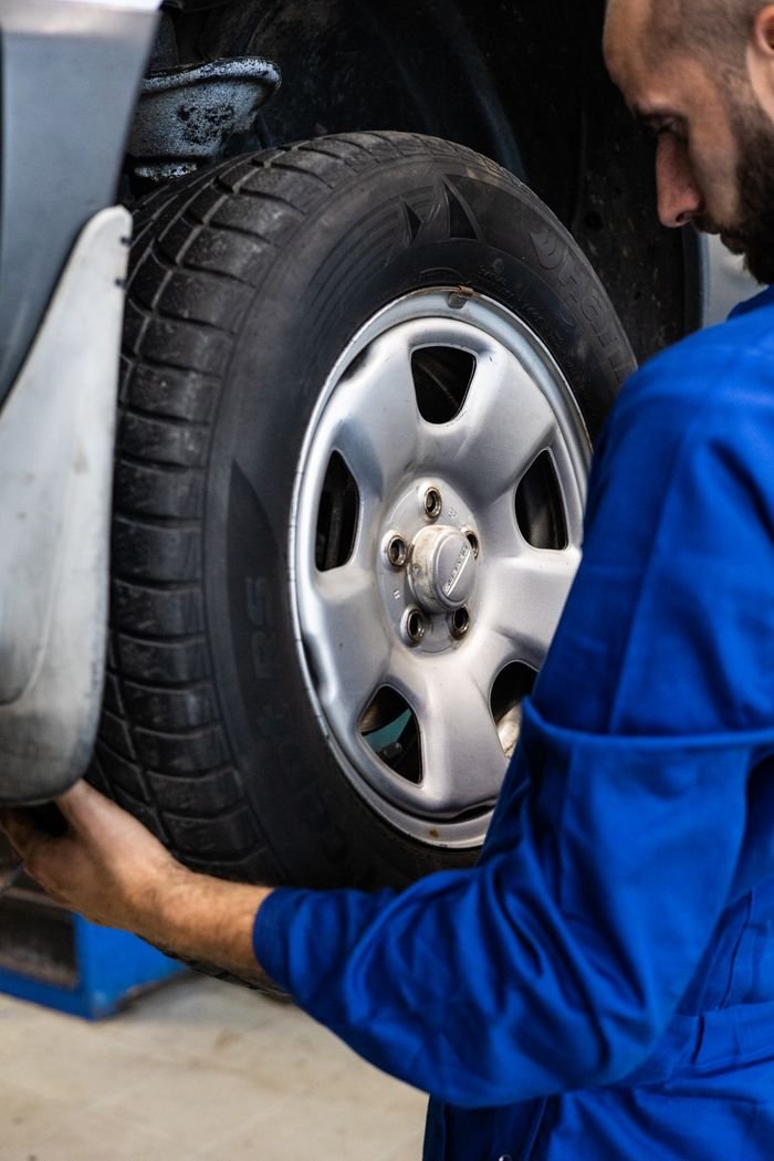 Home A mechanic in blue uniform closely examines a car wheel for repairs.