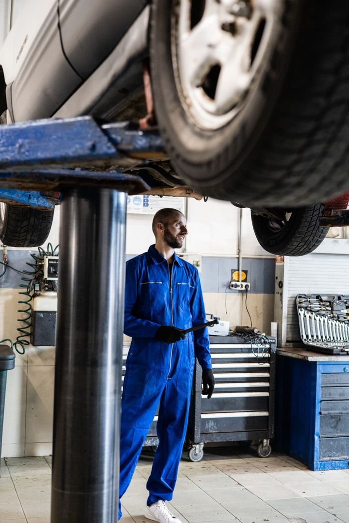 Home Mechanic in blue coverall inspecting vehicle in an auto repair shop. Professional car maintenance concept.