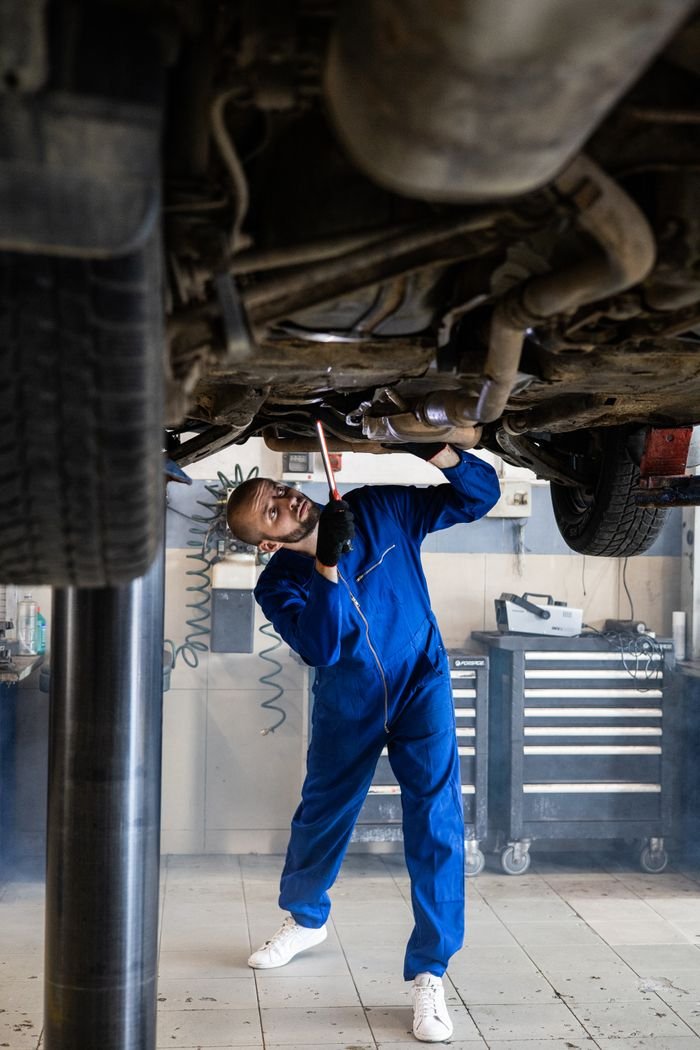 Offerings A female mechanic in blue coveralls inspects a cars undercarriage in an auto repair shop.
